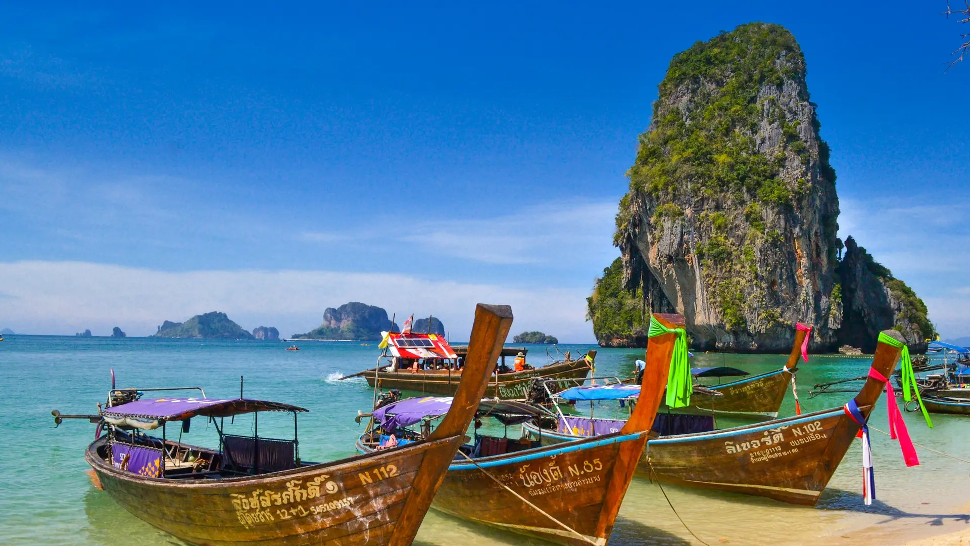 Longtail-både på en strand ved kalkstensklipper i Thailand